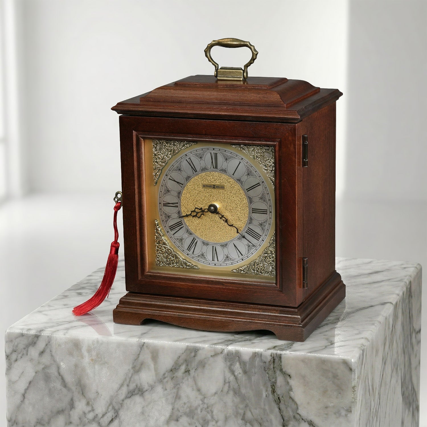 Wooden urn clock with a red tassel on a marble surface