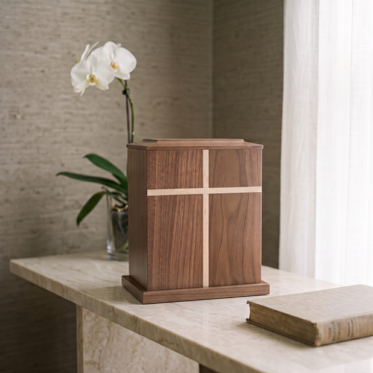 Walnut wood urn chest on a marble table beside a book and a white orchid