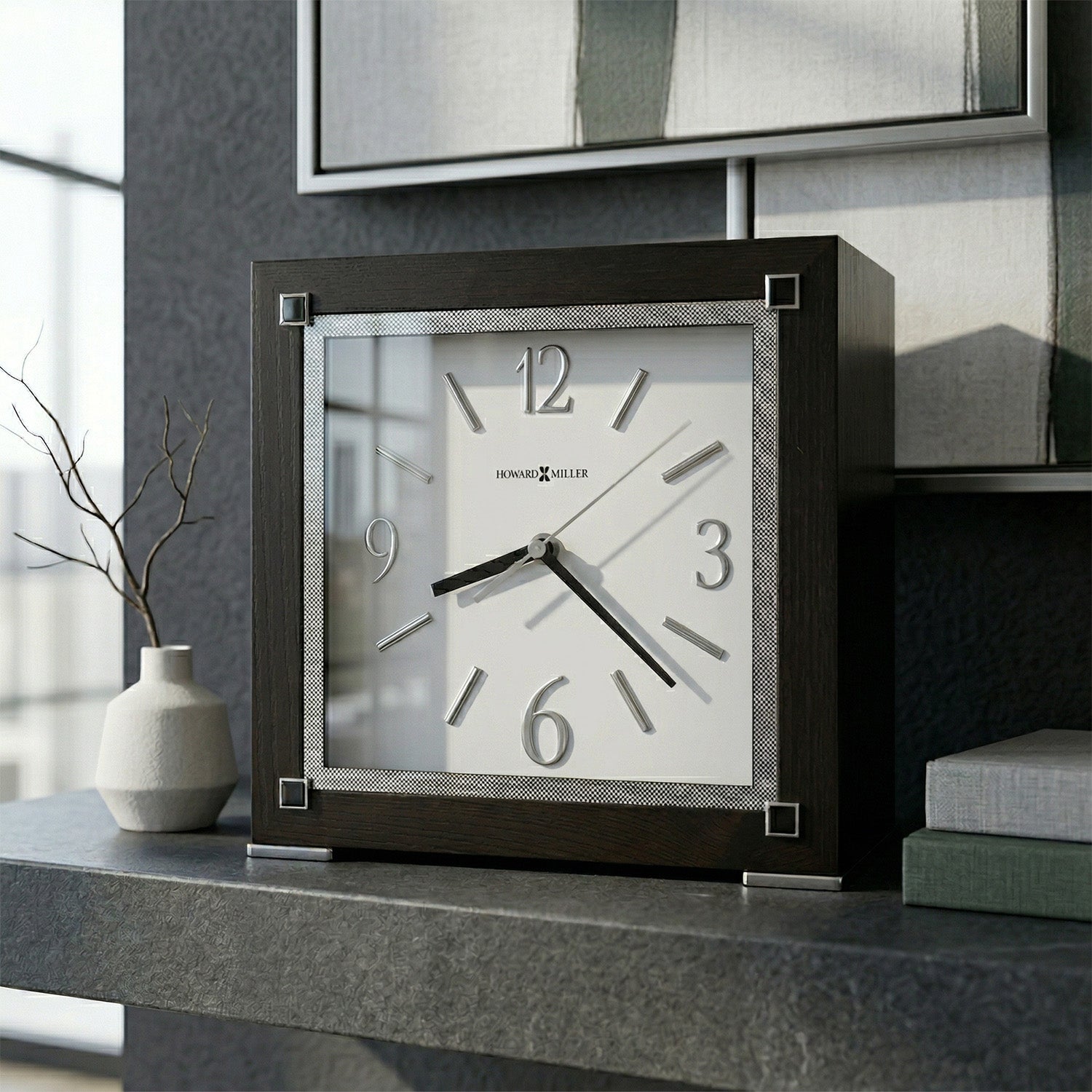 Square urn clock with wooden frame on a surface, with a vase and decorative items in the background.