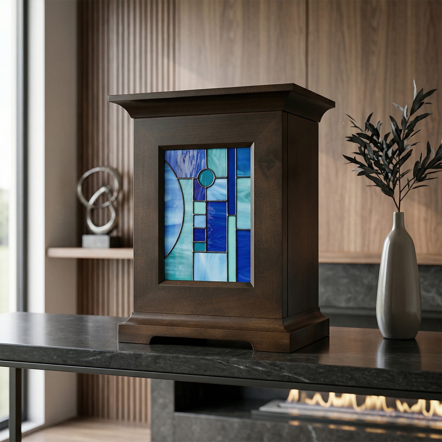 Decorative urn with stained glass panel of a blue shapes on a table in a room with a fireplace.