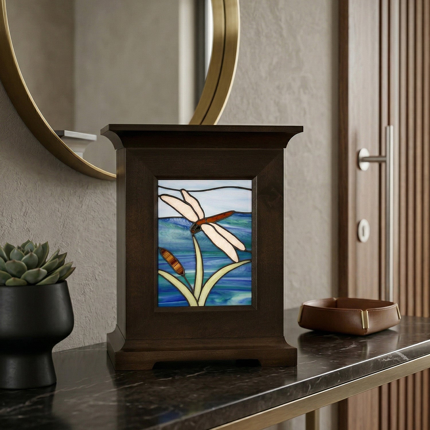Decorative urn with stained glass panel featuring a dragonfly design on a dark marble console table.