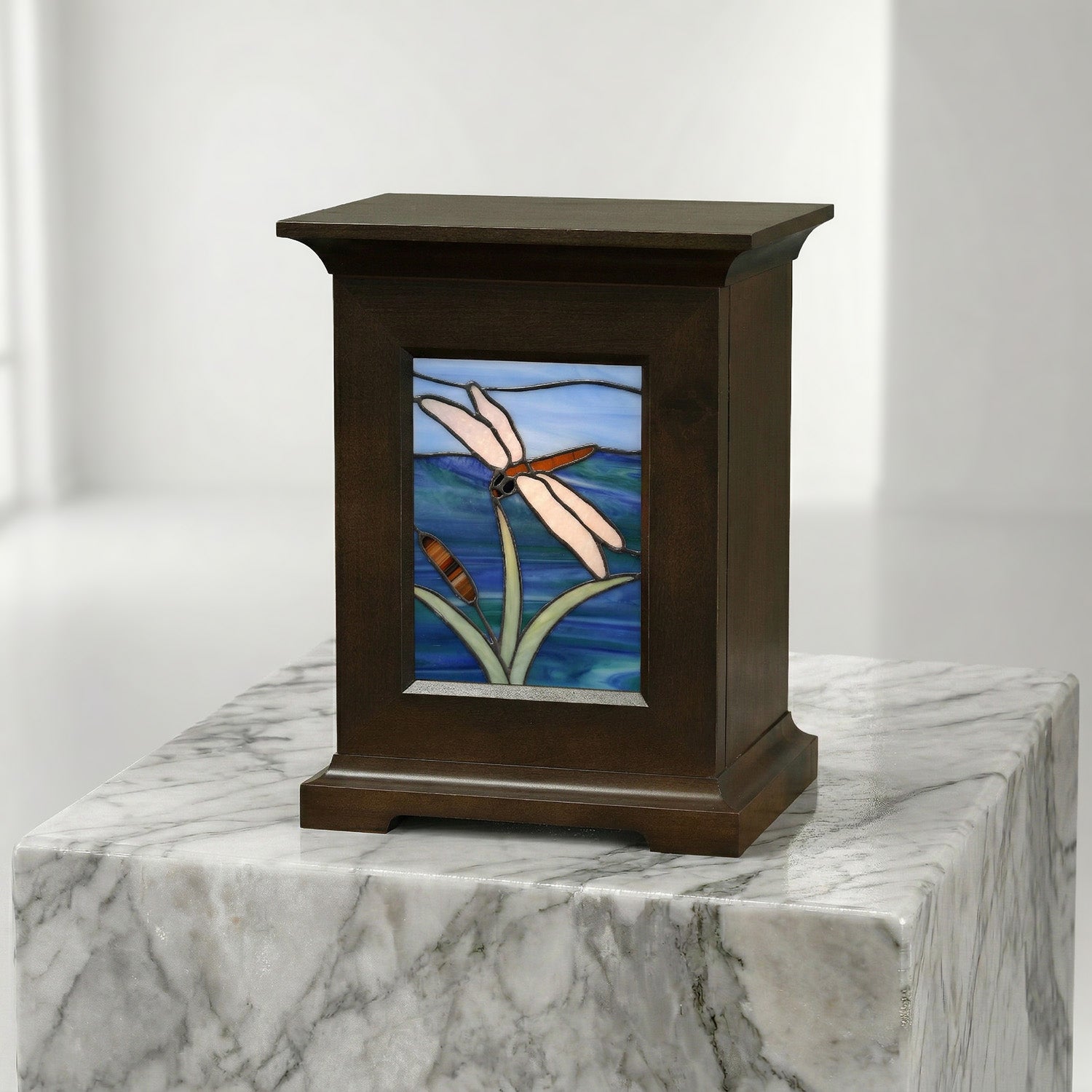 Decorative urn with stained glass panel featuring a dragonfly design on a marble surface.