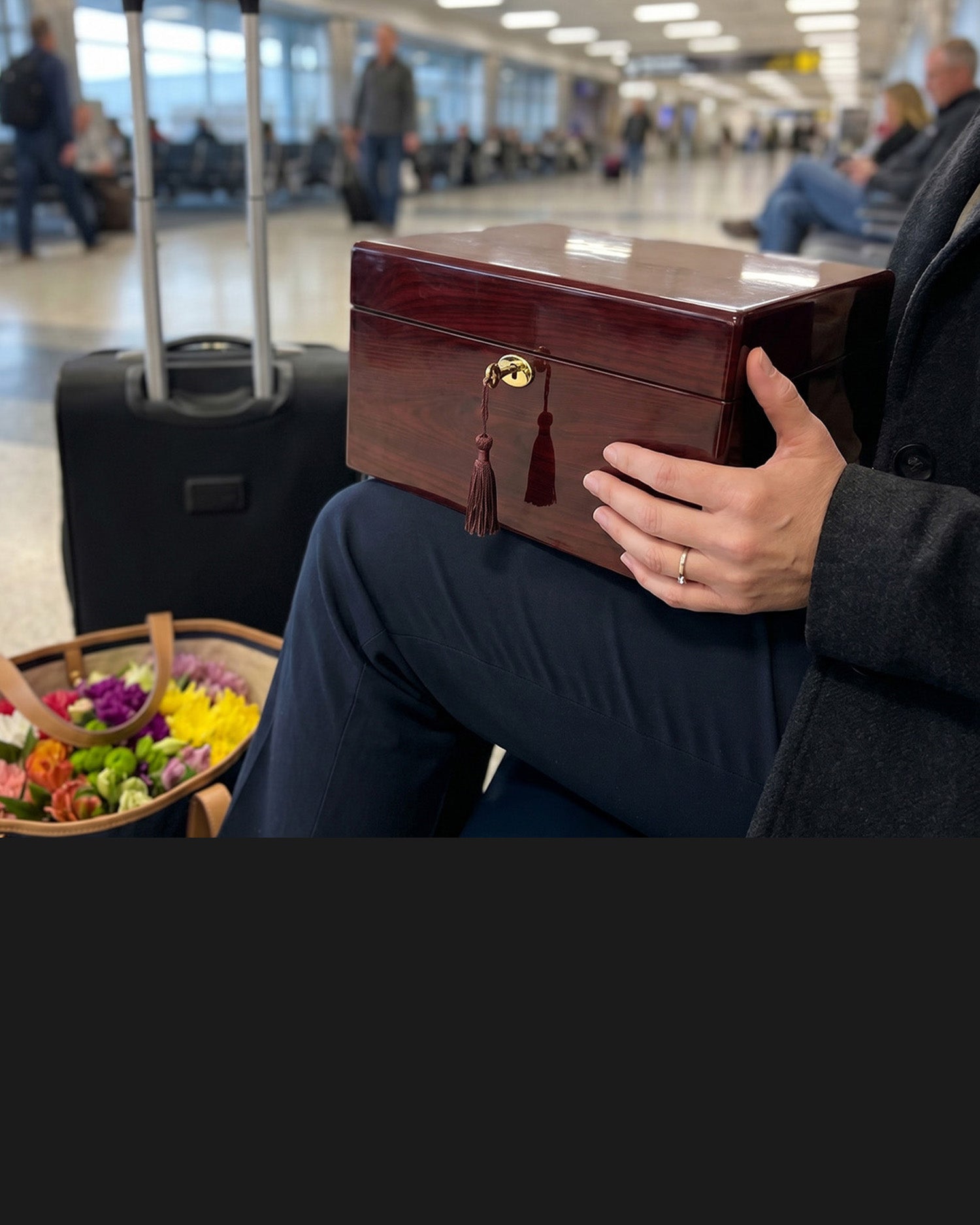 Person holding a wooden box with tassels in an airport setting